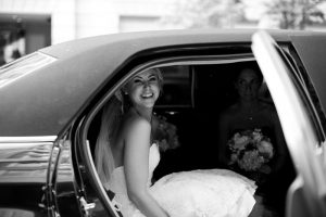 Black and white photo of a bride smiling seated in a limousine